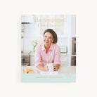 Cover of The Simplified Cookbook - by Emily Ley. A woman in a pink shirt smiles while leaning on a kitchen counter with a mug. The airy kitchen features white cabinets and flowers. Text: Delicious recipes for easy cooking with effortless prep. Brand: Simplified.