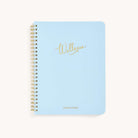 A light blue spiral-bound wellness workbook titled Wellness features elegant gold cursive and the brand Simplified in smaller gold caps at the bottom—ideal for tracking goals and embracing self-care.