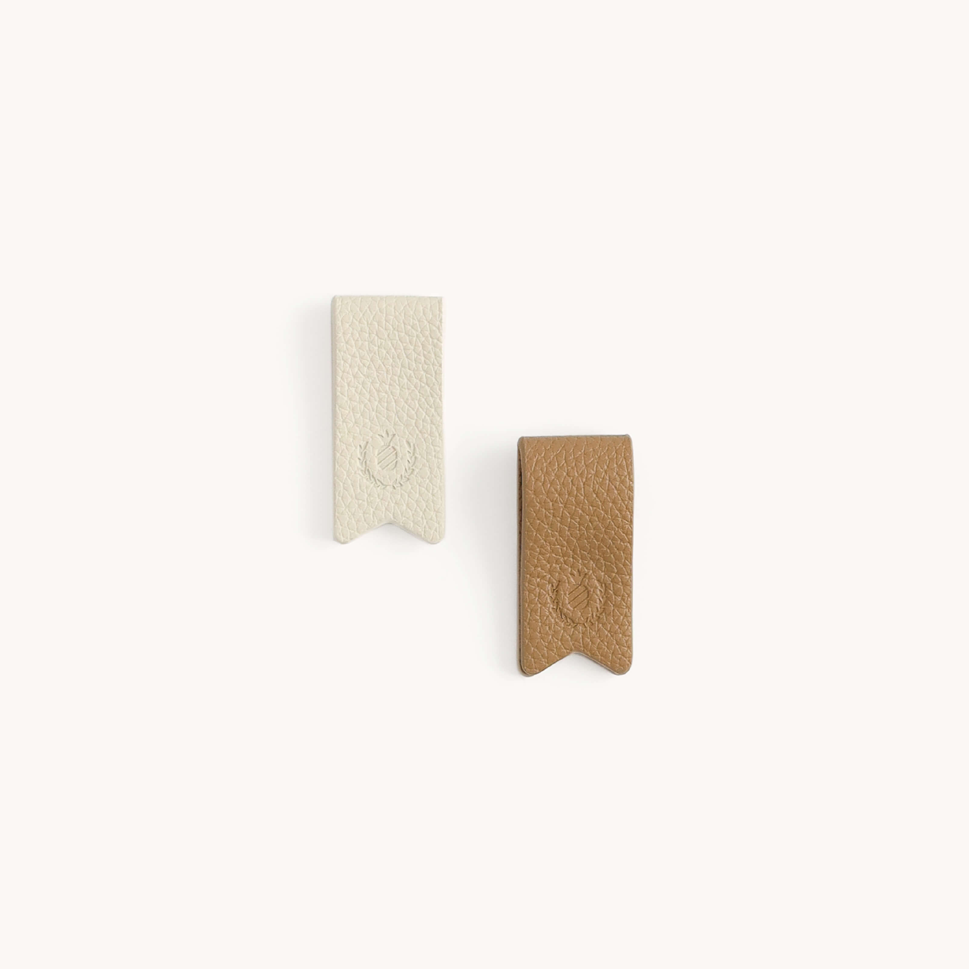 Two leather bookmarks on a plain background, one light beige and the other brown, featuring textured surfaces and small embossed symbols. Perfectly complement your Simplified Cord Organizers - Ivory & Fawn or manage cable clutter with elegance.