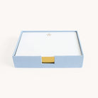 The Desk Jotter - Carolina Linen by Simplified is a square blue linen box with a gold tab, containing gold-gilded notecards featuring a gold wreath emblem. The box is open, showcasing the top card of this refined set.