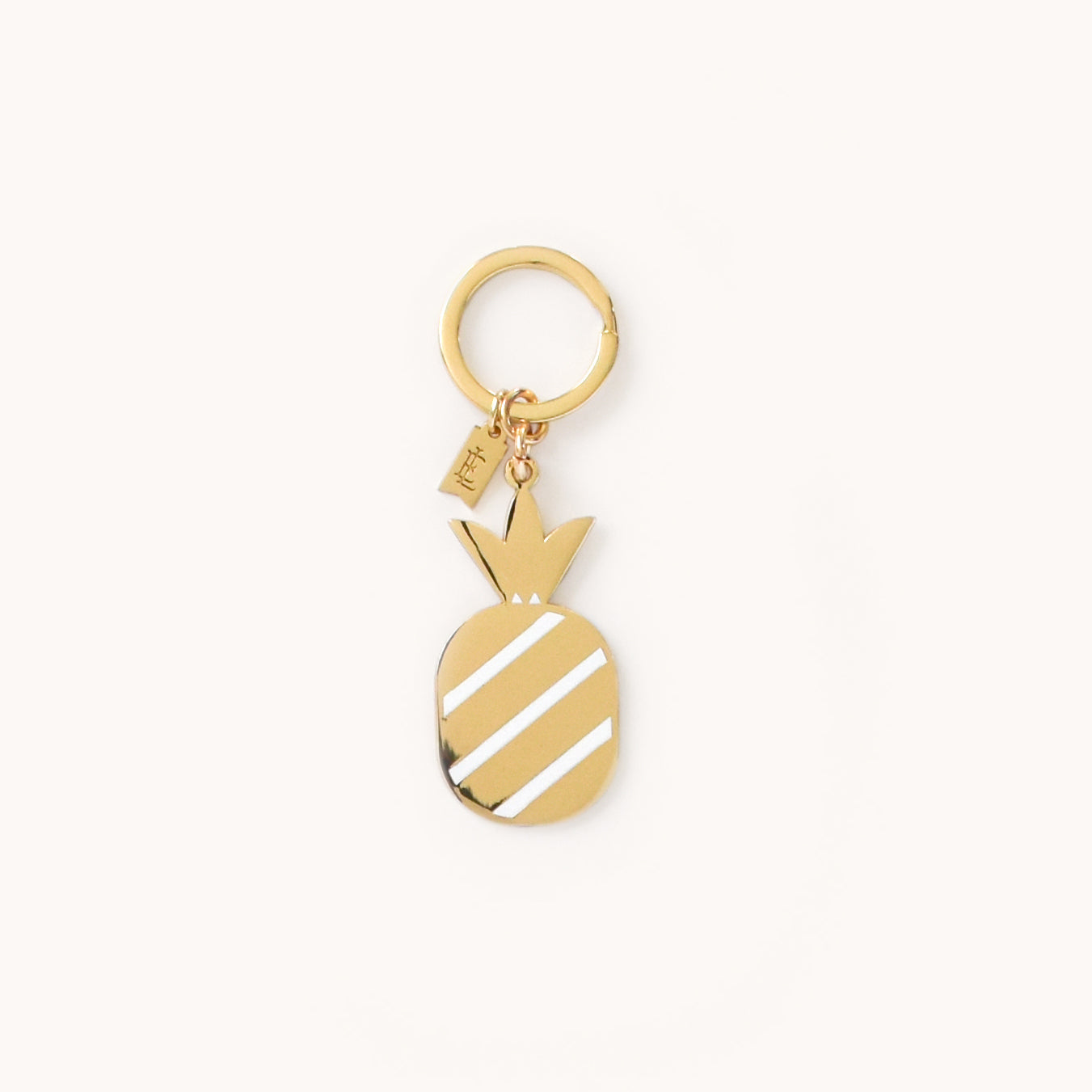 The Simplified Pineapple Key Chain is an elegant gold enamel piece with diagonal white stripes and a small rectangular tag on the ring, showcasing charm and style against a plain white background.