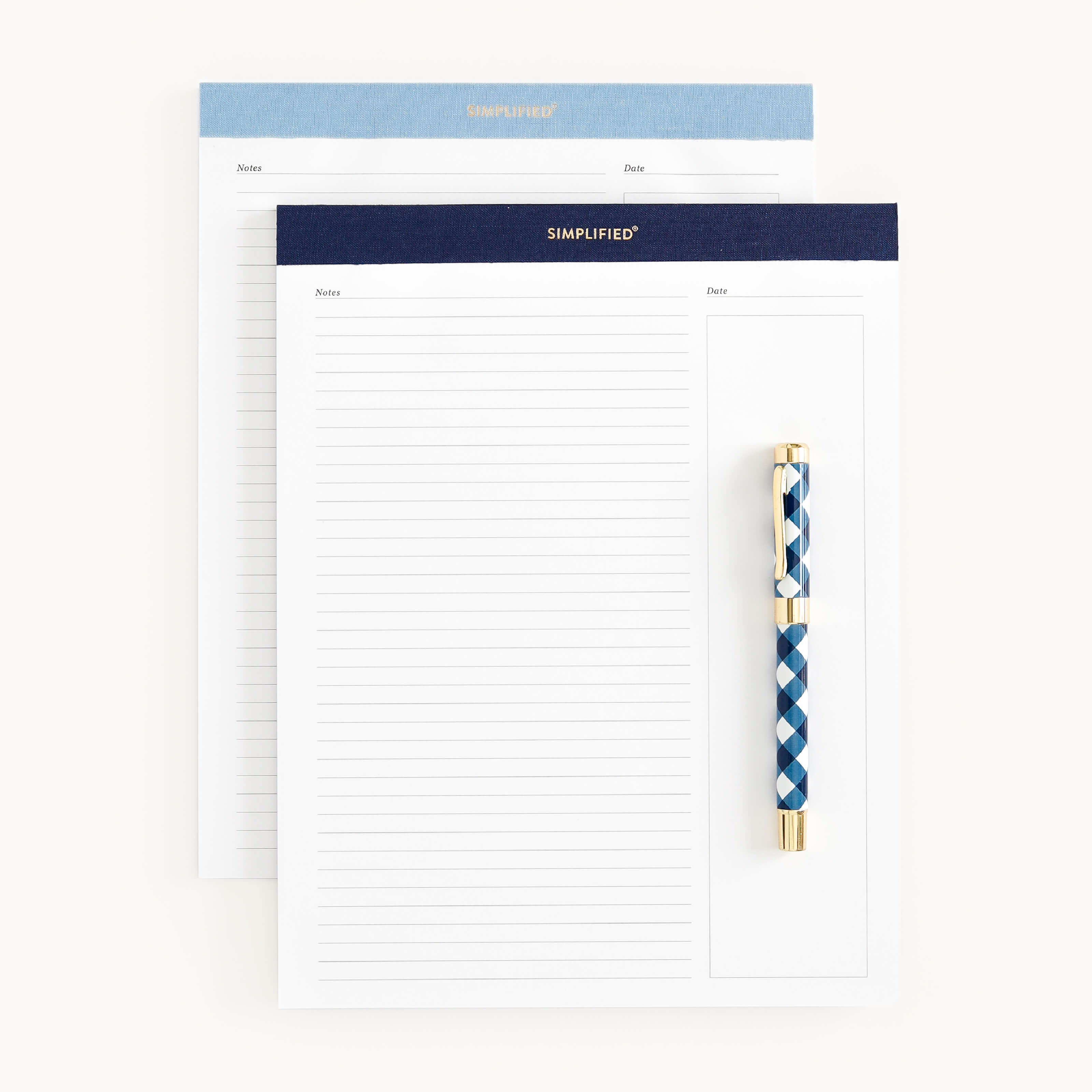 The Legal Pad Set - Navy & Carolina from Simplified includes two pads: one with a blue margin and one navy, both adorned with SIMPLIFIED in gold foil. A blue and gold patterned pen is clipped to the front notepads premium paper, offering style and simplicity.