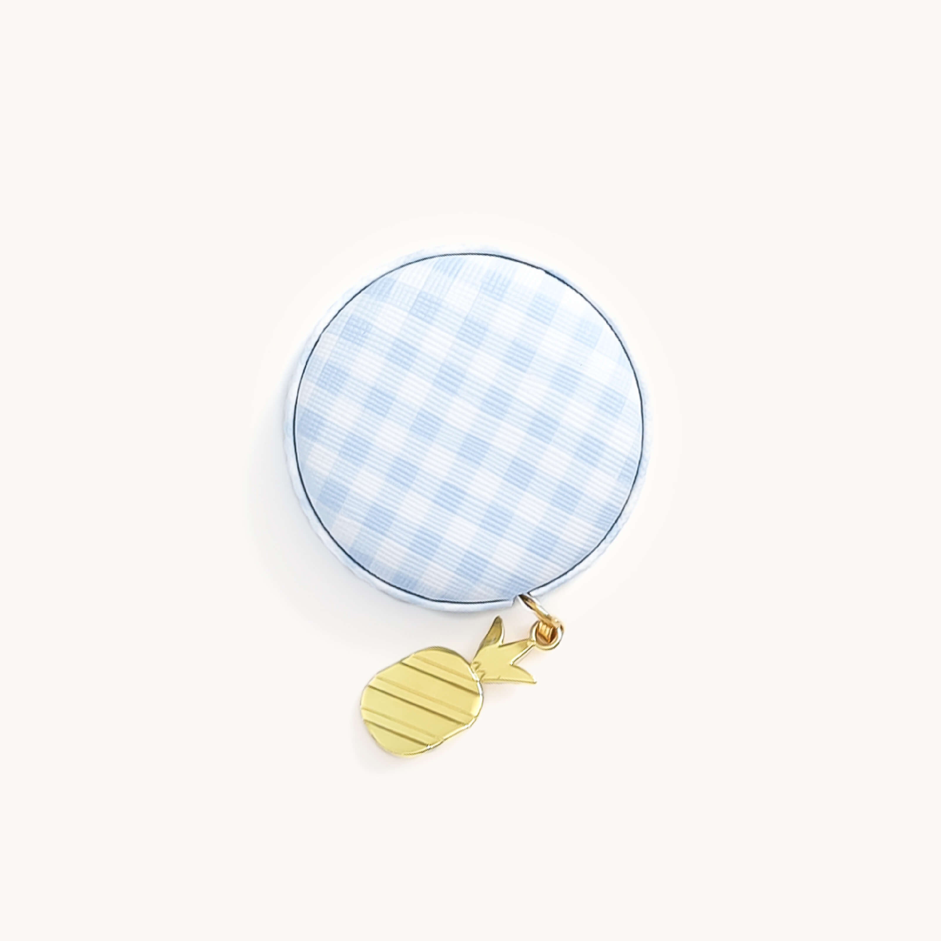 A Simplified purse, showcasing a round blue-and-white checkered design with a gold pineapple charm, includes a compact measuring tape. Set against a plain white background.