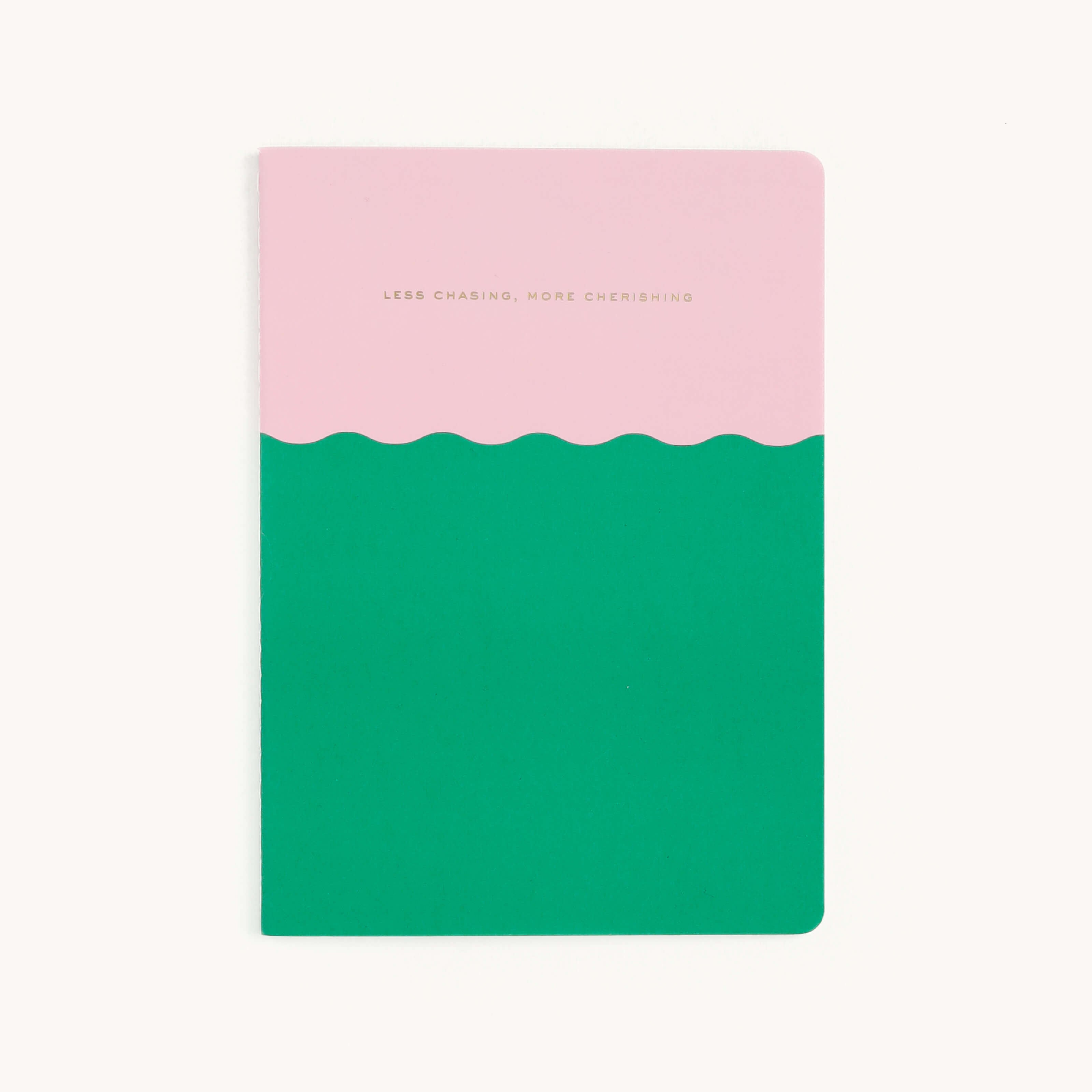 The Simplified Mid-Size Notebook - Less Chasing More Cherishing features an elegant cover with a pink top, green bottom, and wavy divider. The words LESS CHASING, MORE CHERISHING adorn the pink section. It has a plain white background and saddle-stitched binding.