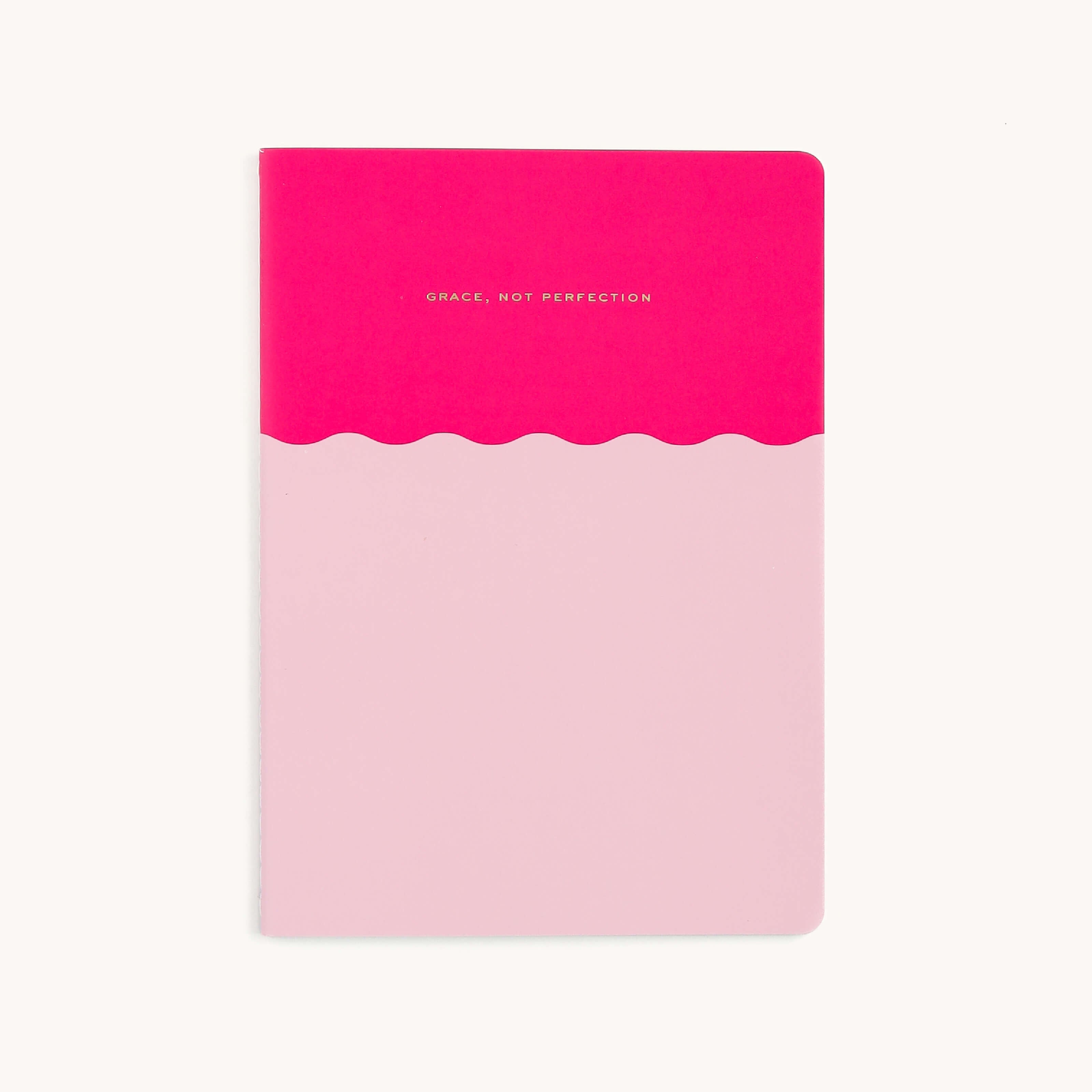 The Simplified Mid-Size Notebook features an elegant design with a pink lower section, red top, and Grace, Not Perfection. A wavy line separates the colors on the plain white background, and the saddle-stitched binding adds sophistication.