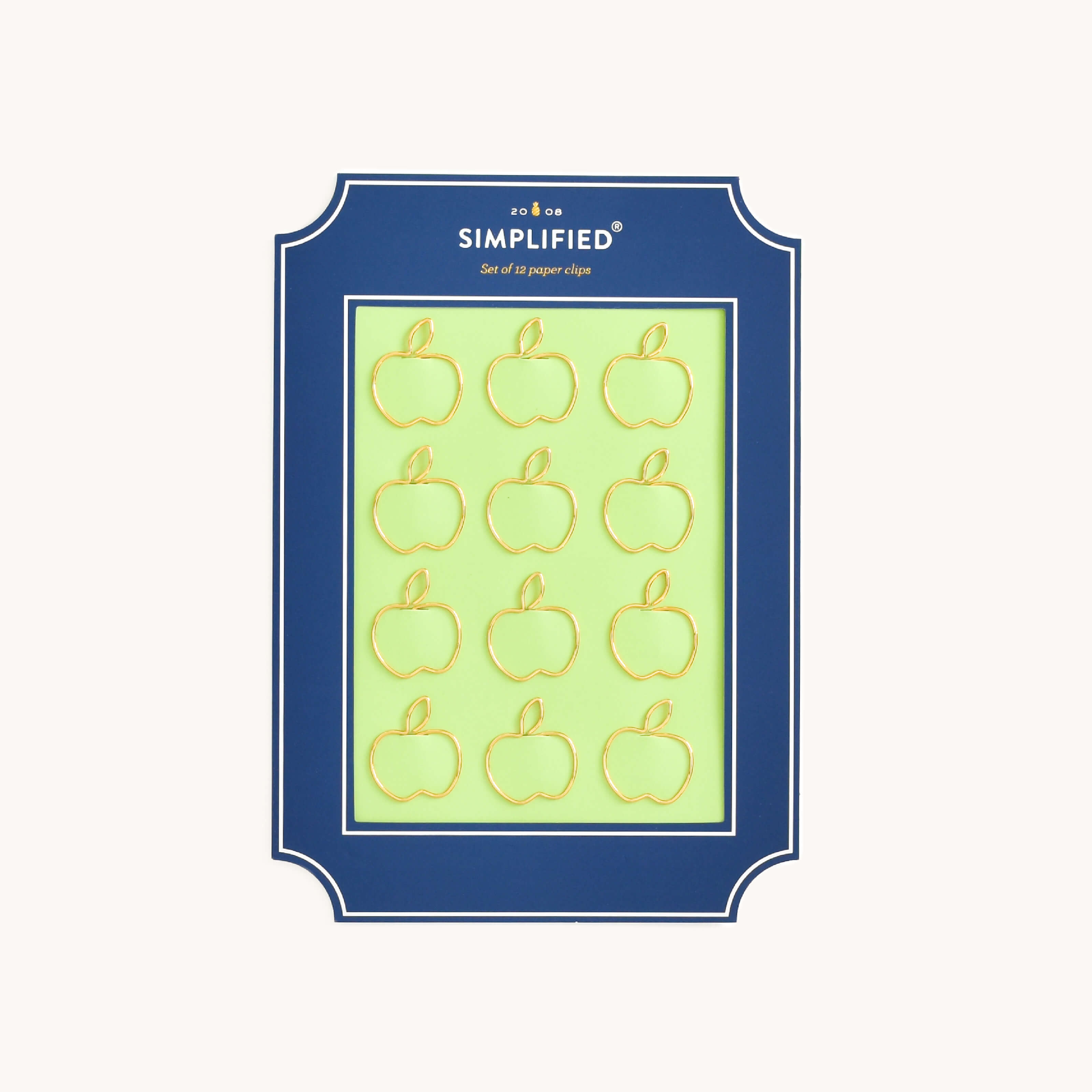 Simplified Apple Paper Clips Set by Emily Ley featuring 12 gold apple-shaped paper clips, packaged on a green backing with a navy frame.