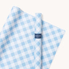 Rolled and unrolled sheets of blue and white checkered gift wrap paper on a plain background, featuring Simplified blue label. Product: Wrapping Sheets - Carolina Gingham by Simplified.