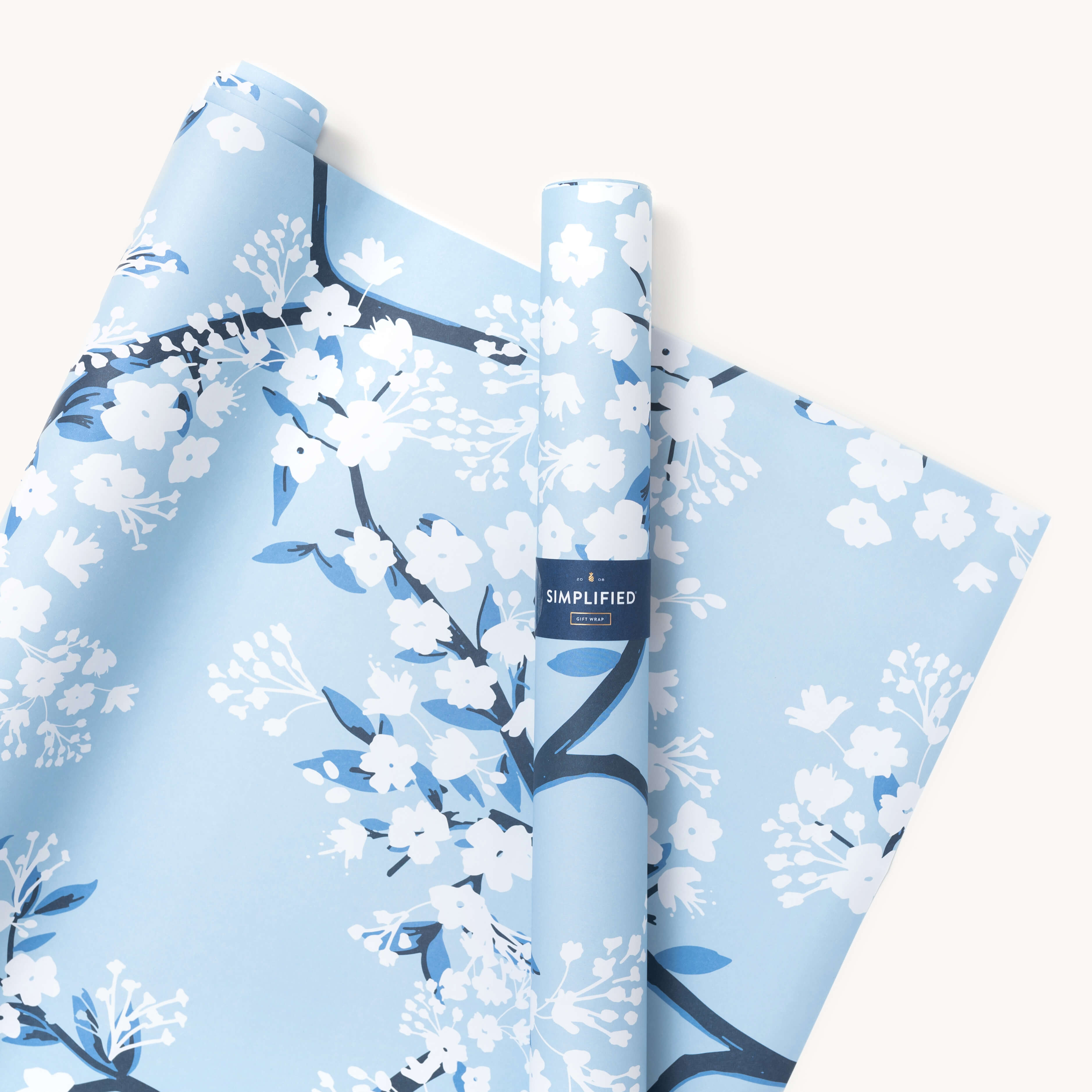 A partially unrolled roll of blue wrapping sheets with hand-painted white flowers and blue leaves reveals a label that reads Simplified.