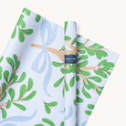 Simplifieds Mistletoe Bows wrapping sheets feature a light blue background with green leafy branches and a hand-painted ribbon design, as indicated by the Simplified label. These gift wraps bring joy to any present.