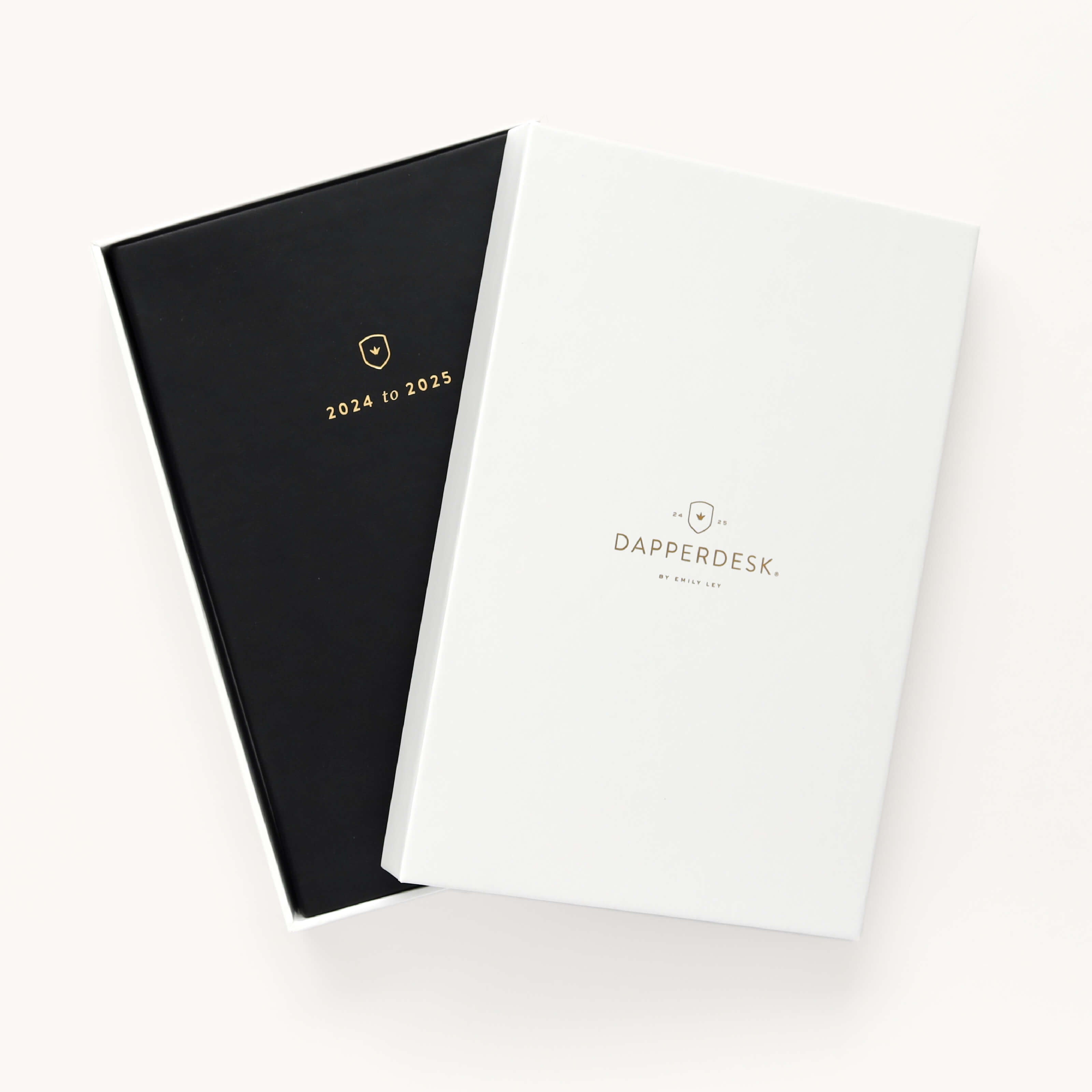 A black and white planner cover overlap slightly. The black one, a 2024-2025 Daily Dapperdesk Planner by Simplified, is sleek with 2024 to 2025 in gold. The white reads Dapperdesk by Ashley Jue above a small emblem, ideal for those seeking a stylish 12-month edition.