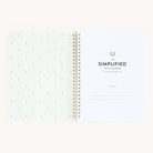 An open spiral-bound Workbook - Hosting by Simplified displays its title on the right page. The left inside cover features a delicate pineapple pattern on a light background, ideal for enhancing memorable gatherings with thoughtful planning.