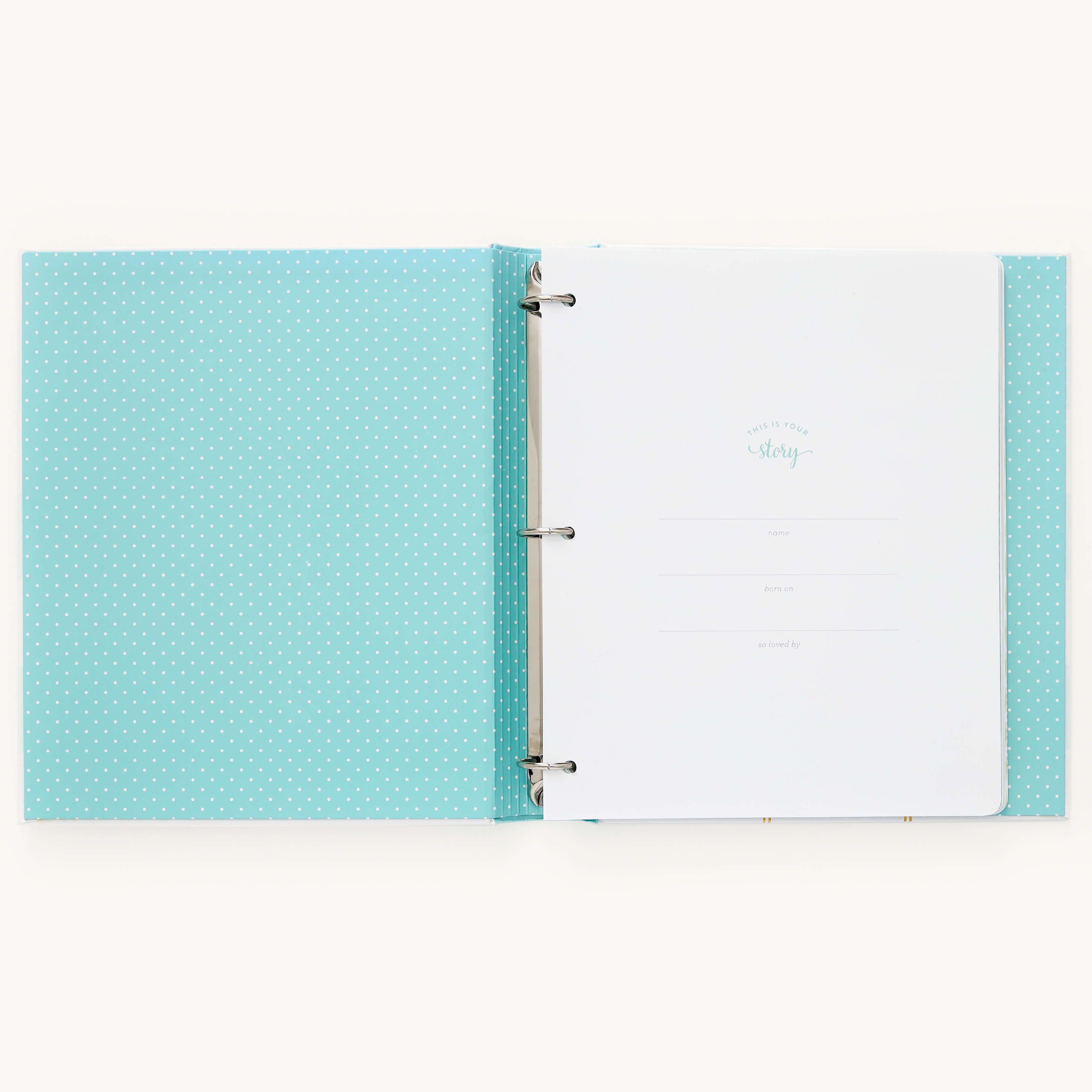 The open Simplified Baby Book - Mint, with a light blue polka dot cover and metal rings, features guided spaces on white pages to document details like name, birthdate, and doctor. Expand memories with customizable page packs in this delightful baby book.