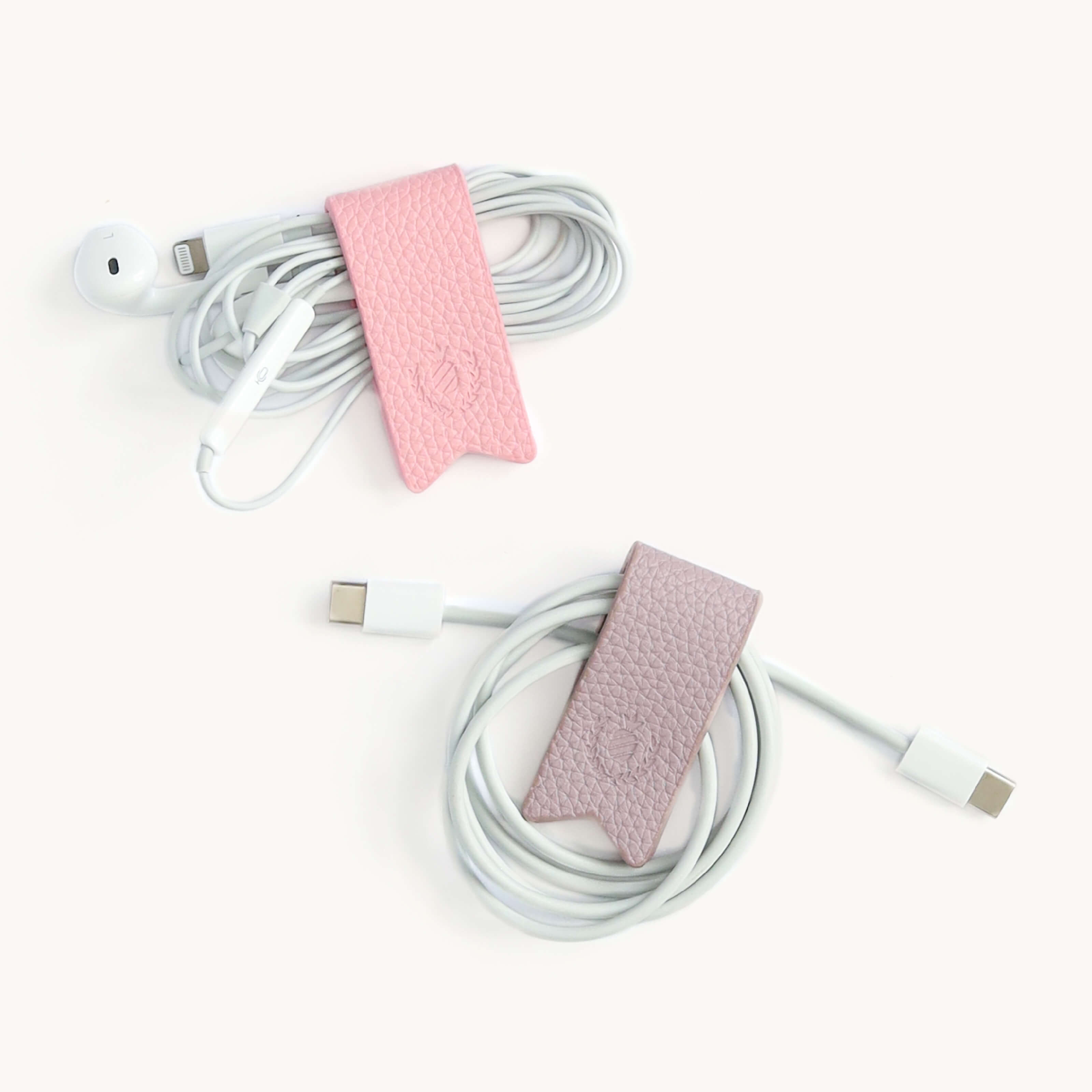 Two sets of earbuds and charging cables are neatly wrapped with Simplifieds Cord Organizers in Blush & Lilac on a white background, effortlessly eliminating cable clutter.