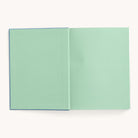 A Bullet Journal - French Blue from Simplified, featuring a plain light green cover and matching dot-grid pages, lies flat on a neutral background, highlighting its minimalistic design.