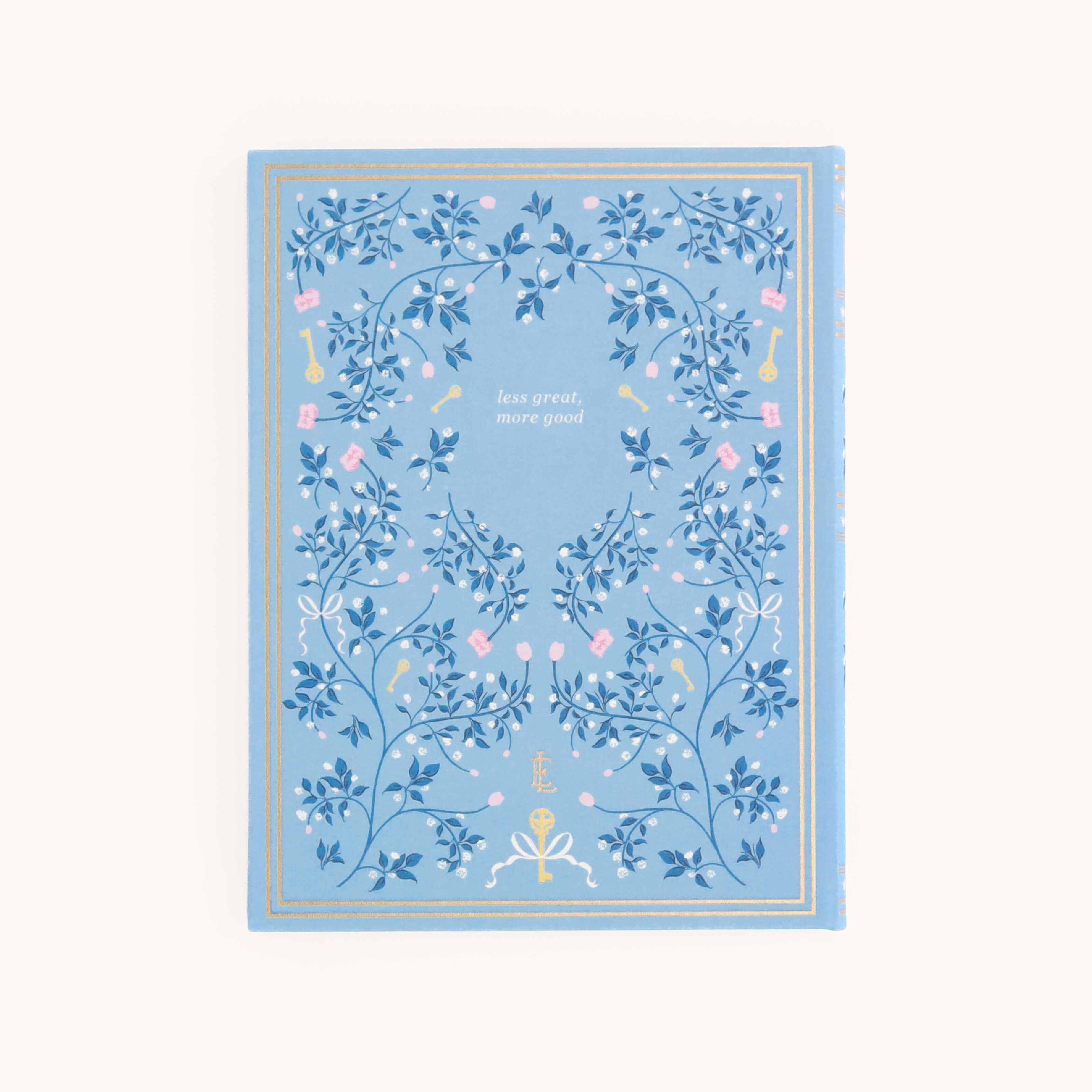 The Linen Journal - Carolina by Simplified is a blue notebook featuring decorative floral patterns and gold accents. Ideal for capturing reflections and creativity, it has the phrase less great, more good in the center.