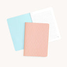 Two Simplified mini notebooks are shown: one open with a light blue cover and blank lined pages, and another closed featuring the Cabana Pinstripe design with custom orange and white stripes, set against a plain white background.