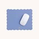 A white computer mouse sits on a light blue Scalloped Mousepad by Simplified, featuring a small golden emblem at the bottom center. It serves as a stylish desk accessory against an off-white background.