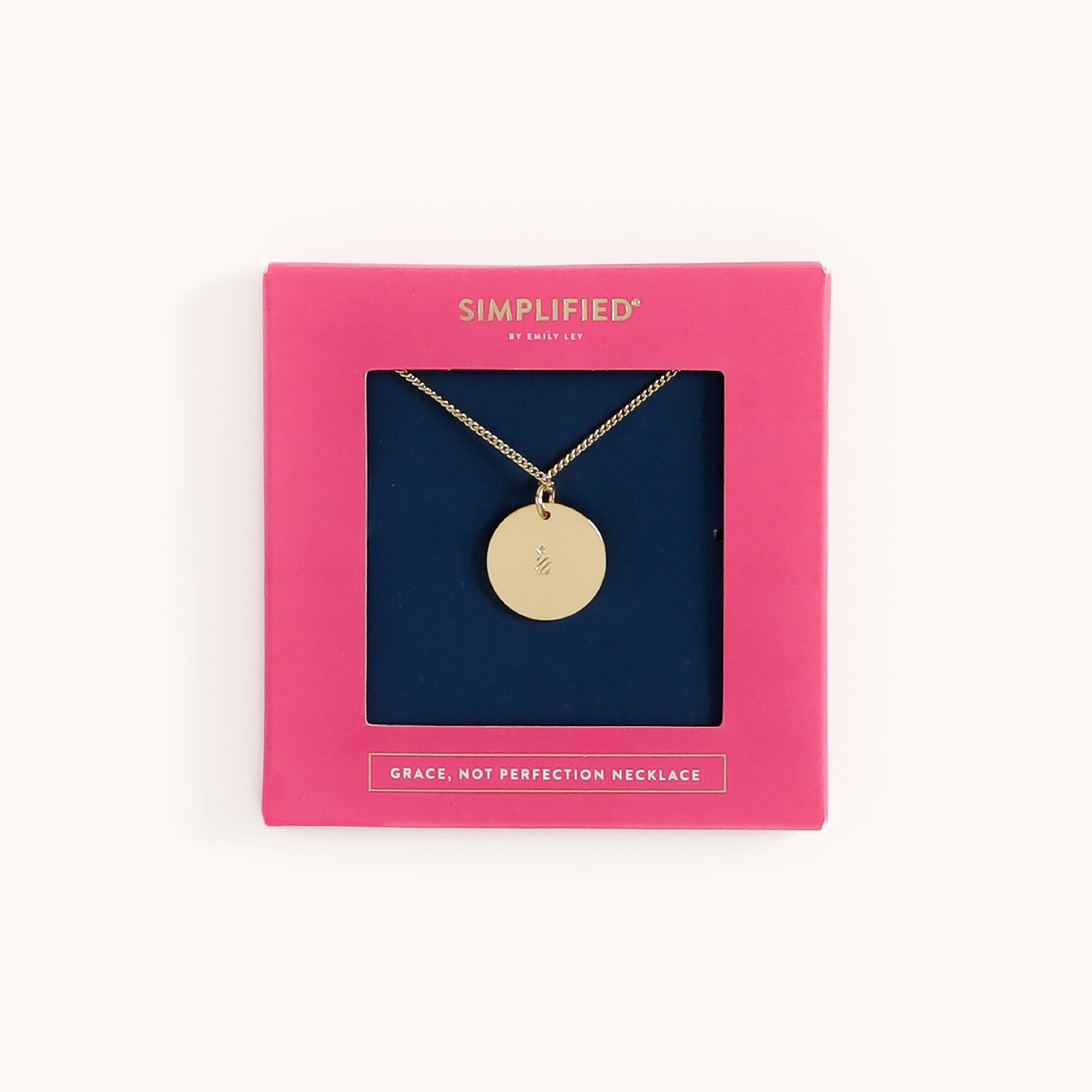 The Grace Not Perfection gold necklace from Simplified exudes elegance with its circular pendant. Its presented in a pink gift box with a dark blue interior, adorned with SIMPLIFIED and GRACE, NOT PERFECTION NECKLACE.