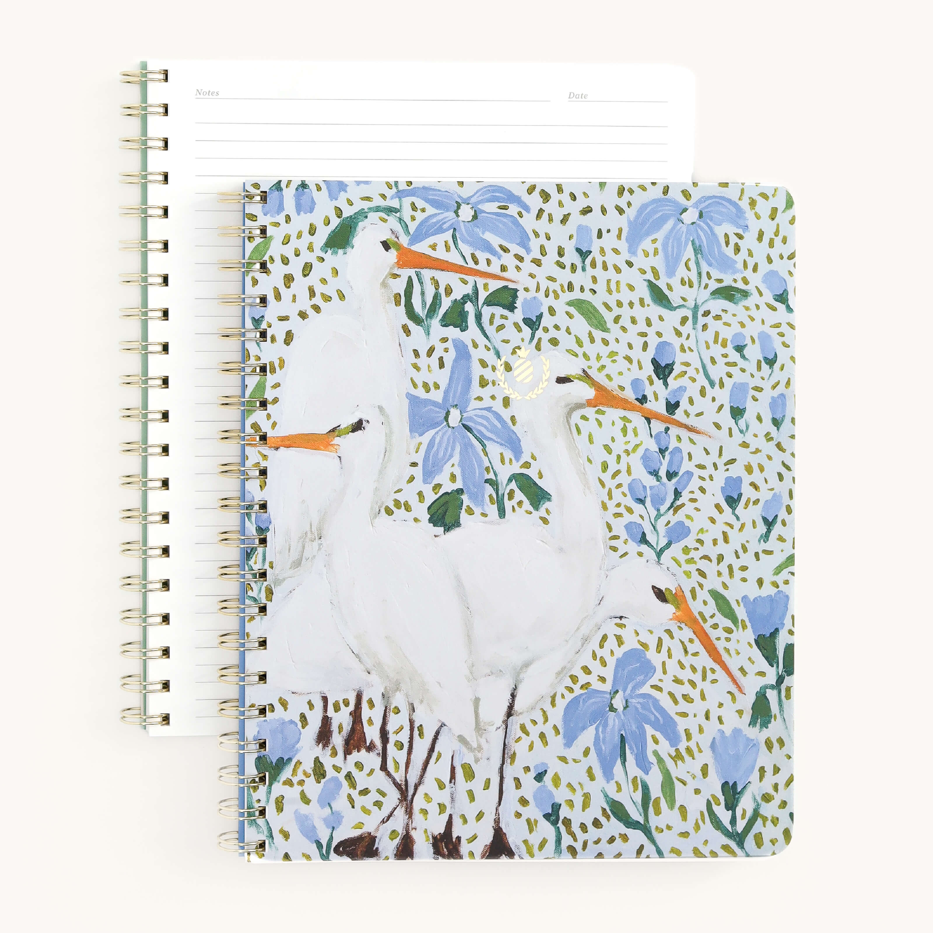 The Notebook - Beaufort Birdies by Simplified is a spiral-bound classic with a soft-touch cover, displaying white herons among blue flowers and green leaves. Another notebook beneath shows gold wire-o binding and lined paper with Notes and Date headings.