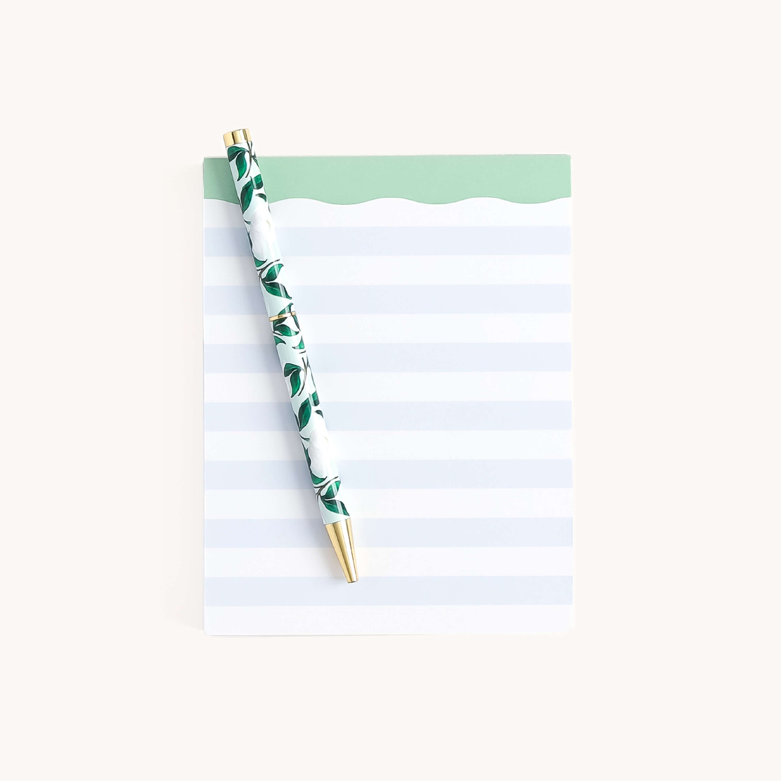 The Simplified Notepad - Blue Stripes with a green top edge lies on a plain surface. A floral pattern pen with a gold tip rests diagonally across it, ready to organize your thoughts or jot down notes in style.