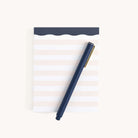 A navy blue pen rests diagonally on the Simplified Notepad - Cream Stripes, featuring an elegant, minimalist design with light lines on a white background, perfect for jotting down reminders or organizing thoughts.