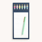 The Tall Notepad - Nutcrackers by Simplified features colorful Happy Stripe Nutcrackers at the top. Accompanied by a light green pen with a gold clip, it rests diagonally on the magnetic pad against an off-white backdrop.