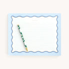 The Simplified Notepad - Scallop Lined (8 x 10) has a blue scalloped border and Take Note header on lined paper. A pen with leafy green and gold foil accents complements it against a neutral backdrop.