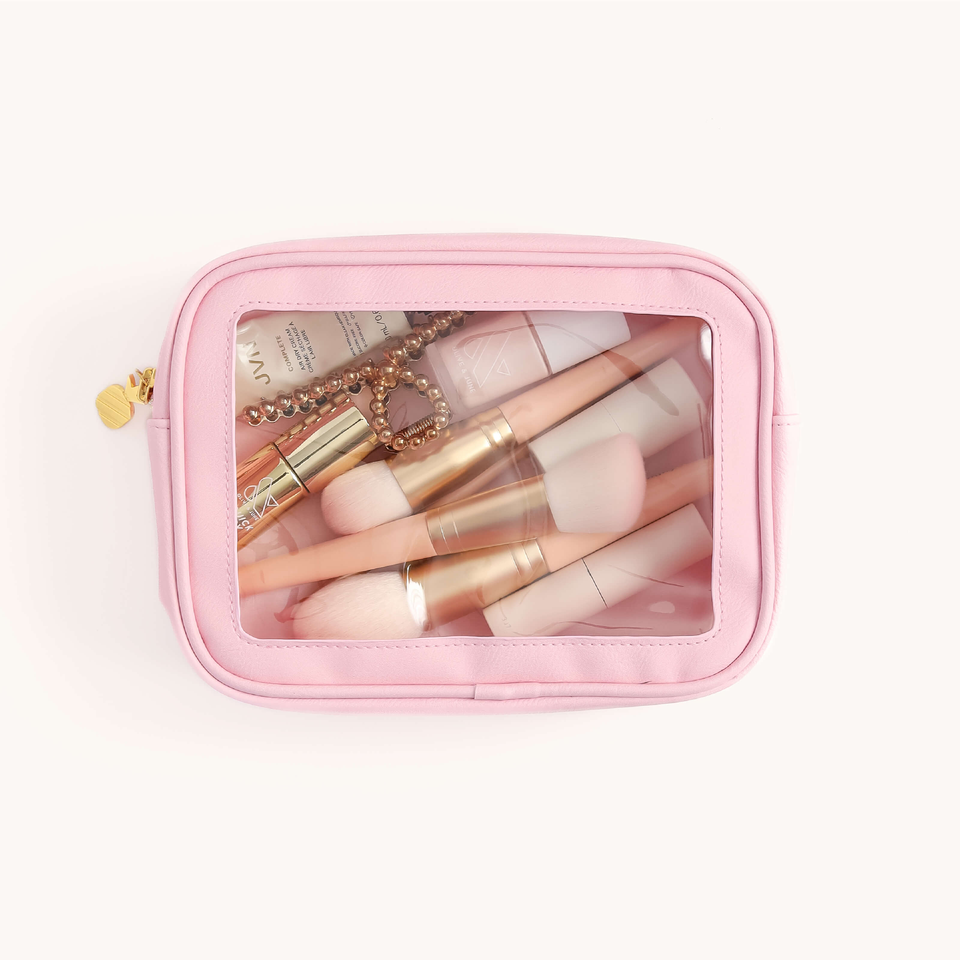 The Leatherette Travel Bag - Blush by Simplified is perfect for travel, showcasing makeup brushes, lipsticks, a compact, and a star charm necklace through its clear window. Its gold zipper pull adds elegance while ensuring TSA-friendly access and organization for essentials on the go.