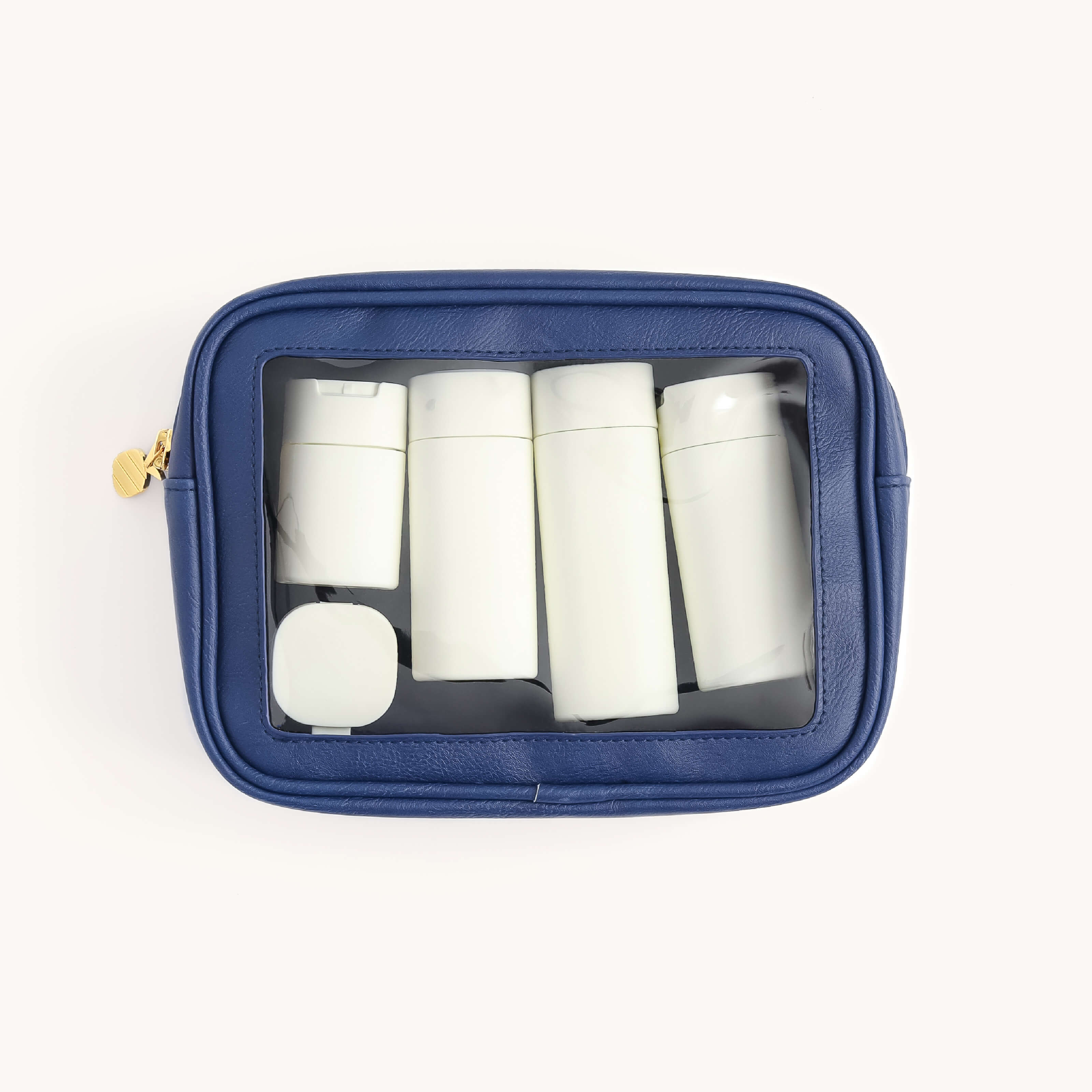 The Simplified Leatherette Travel Bag - Navy showcases five white bottles and a square container inside its transparent front. Ideal for organizing items, it features a gold zipper on the left side against a plain white background, making it TSA-friendly for travel.