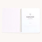 An open spiral-bound workbook by Simplified features vertical light pink stripes on the left and Workbook - Meal Planning with Belongs to lines for personal info on the right. Ideal as a meal planner, its rounded-corner pages invite you to begin your grocery shopping journey.