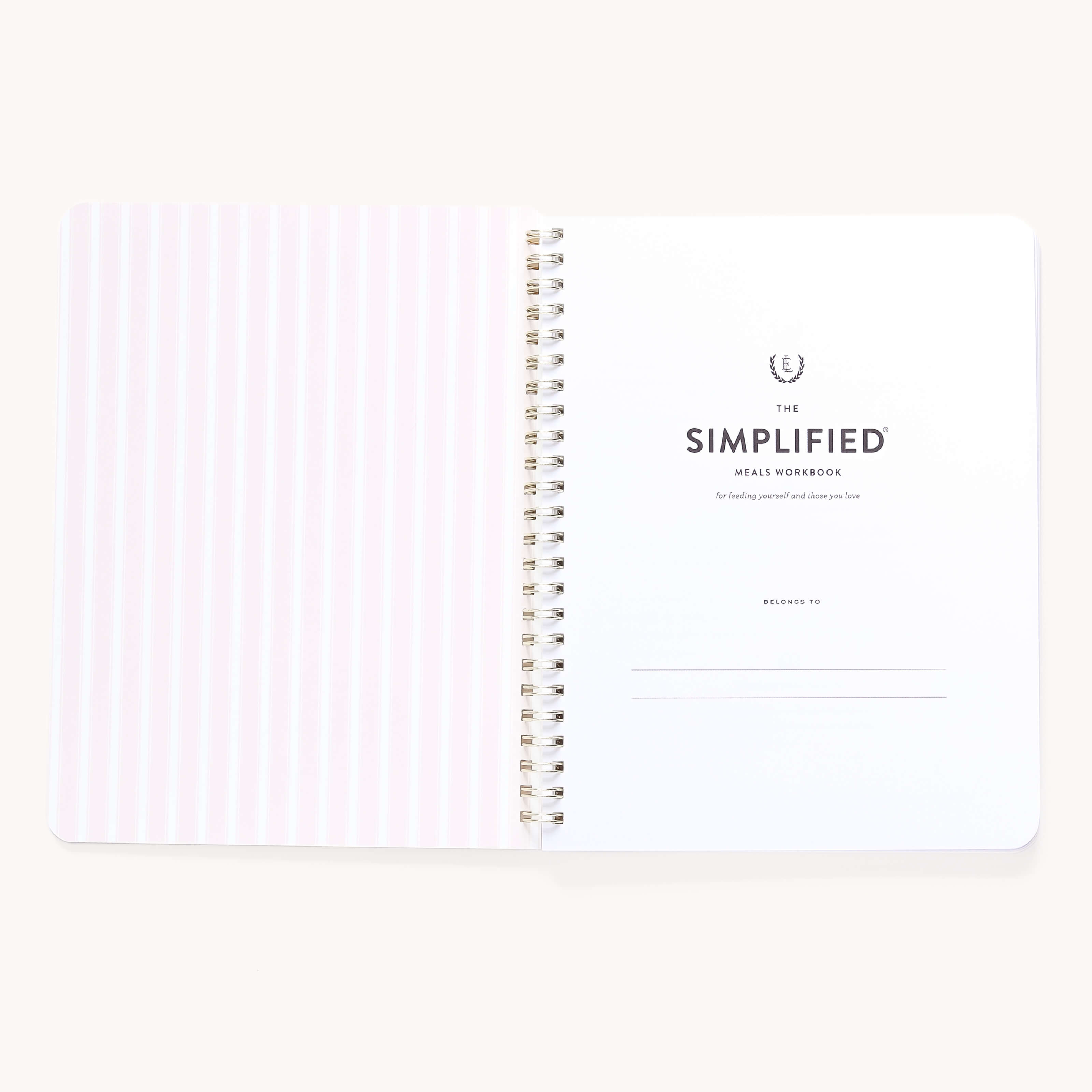 An open spiral-bound workbook by Simplified features vertical light pink stripes on the left and Workbook - Meal Planning with Belongs to lines for personal info on the right. Ideal as a meal planner, its rounded-corner pages invite you to begin your grocery shopping journey.