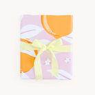 A rectangular gift wrapped in Simplifieds Wrapping Sheets - Blush Oranges, featuring pastel pink hues with orange and white abstract shapes, tied with a pale yellow ribbon for a vibrant and joyful touch on a light background.