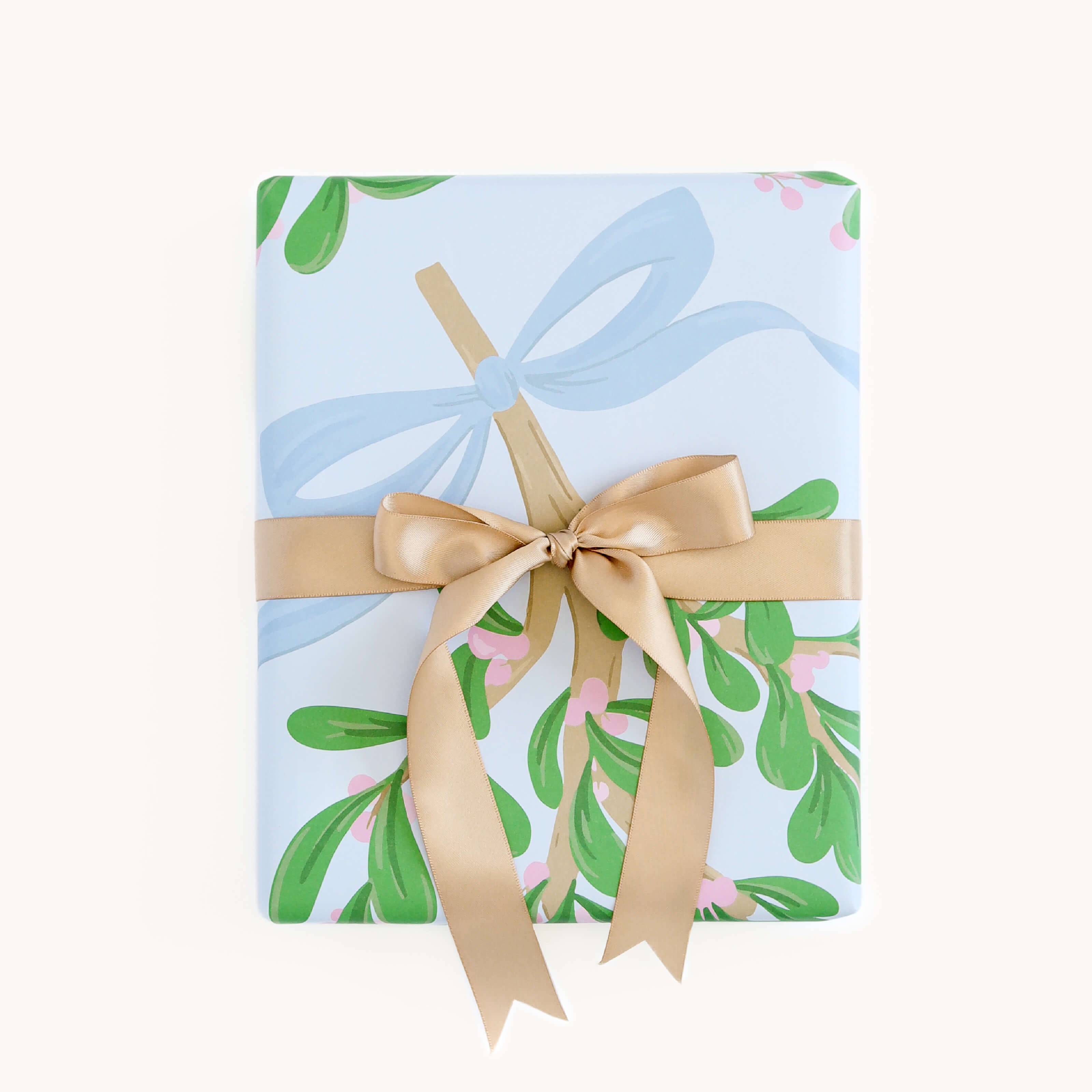 A gift wrapped in Simplifieds Mistletoe Bows paper, featuring white sheets with cheerful green and pink floral designs, tied with a gold ribbon and bow.