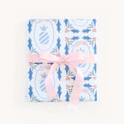 The gift, wrapped in Simplifieds Wrapping Sheets - Pineapple Stamps, flaunts a vibrant blue and pink floral and striped pattern. A light pink ribbon is tied in a bow, adding flair to the lively design, while the plain white background enhances the colorful wrap.