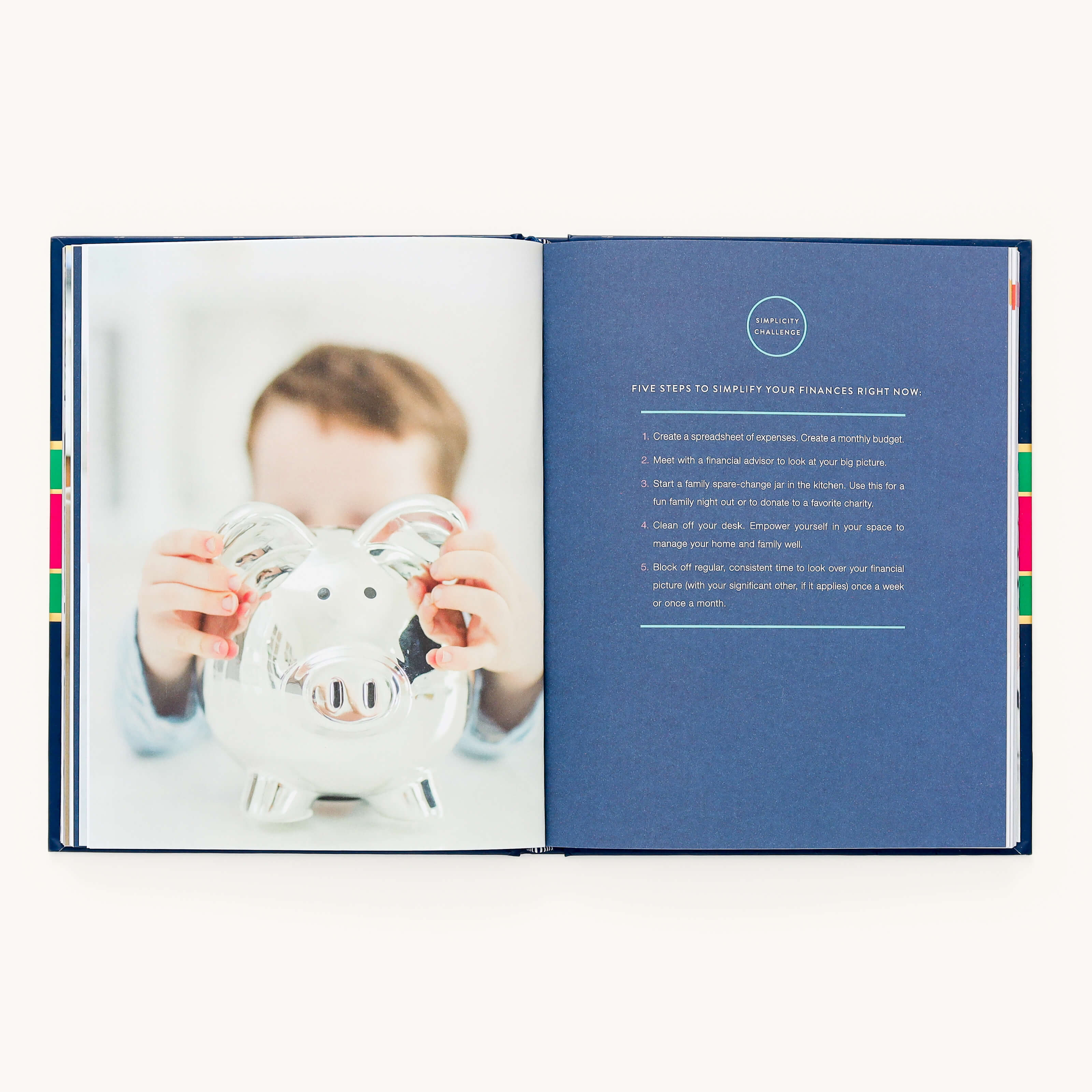 The open book, A Simplified Life by Emily Ley (Simplified), shows a blurred photo of a child with a piggy bank on the left and practical tips titled Five Steps to Simplify Your Finances Right Now on the right, all wrapped in an inviting navy blue cover for financial clarity.