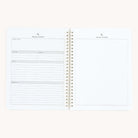 The Workbook - Project Management by Simplified is an open spiral-bound notebook featuring a left page with form sections for project name, timeline, budget, details, and address. The right page is blank for notes or sketches. It sits against a plain off-white background.