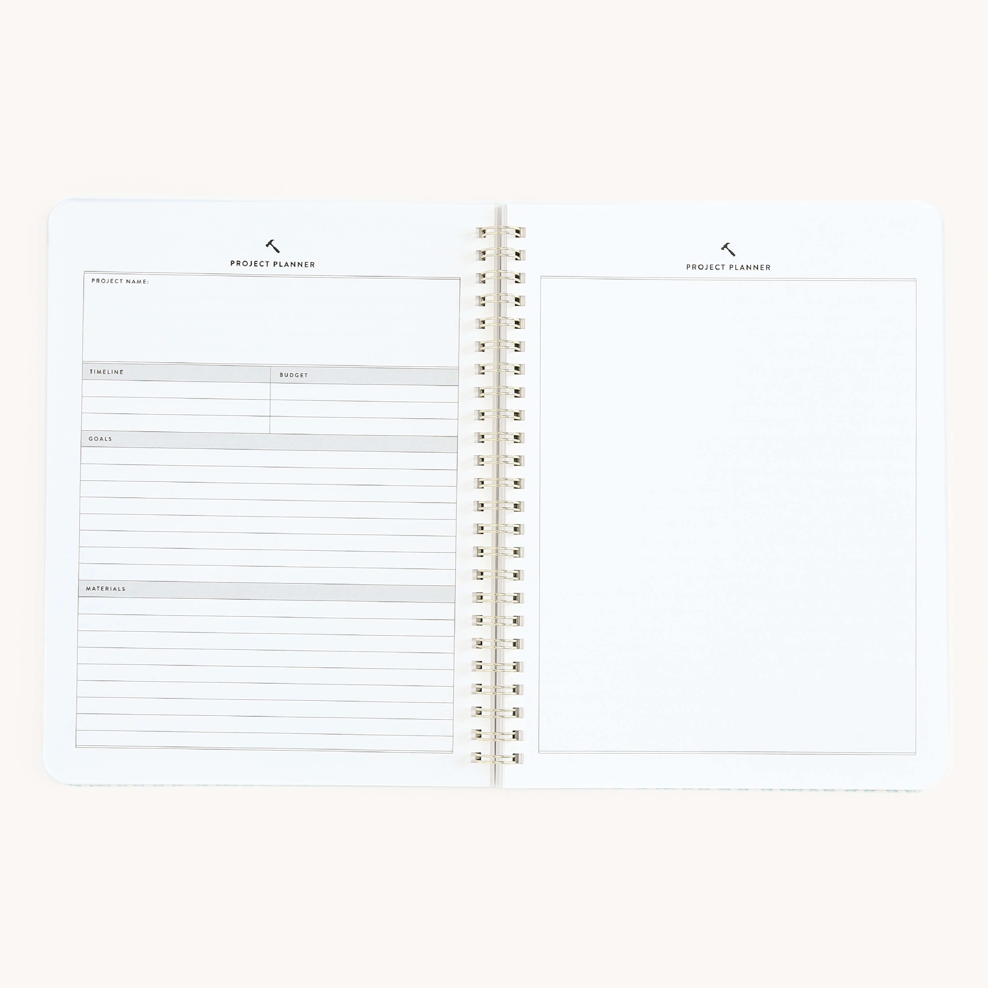 The Workbook - Project Management by Simplified is an open spiral-bound notebook featuring a left page with form sections for project name, timeline, budget, details, and address. The right page is blank for notes or sketches. It sits against a plain off-white background.