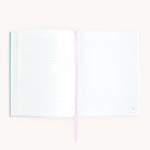 The open Linen Journal - Blush by Simplified, with lined pages and a pink ribbon bookmark, lies flat on a light surface, inviting creativity. Its off-white pages invite reflection, while the partially visible cover hints at countless unwritten entries.