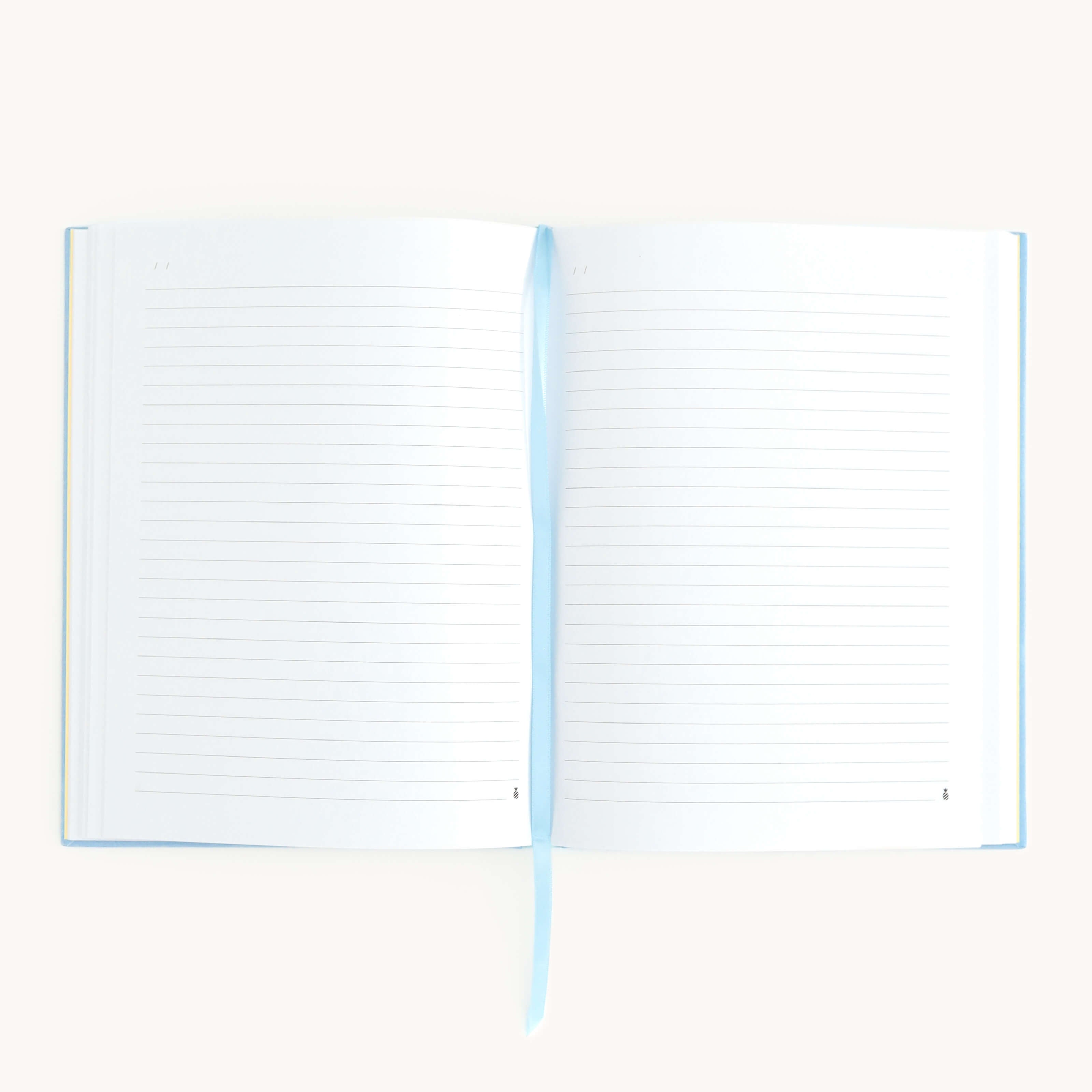 On a white surface, the Linen Journal - Carolina by Simplified invites creativity with its open lined pages and a light blue ribbon bookmark marking moments of reflection.