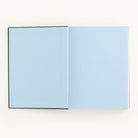 The Grace Linen Journal by Simplified elegantly displays blank, light blue pages on a plain white background. Its linen hardcover enhances the serene design, providing an ideal space for your thoughts and dreams.