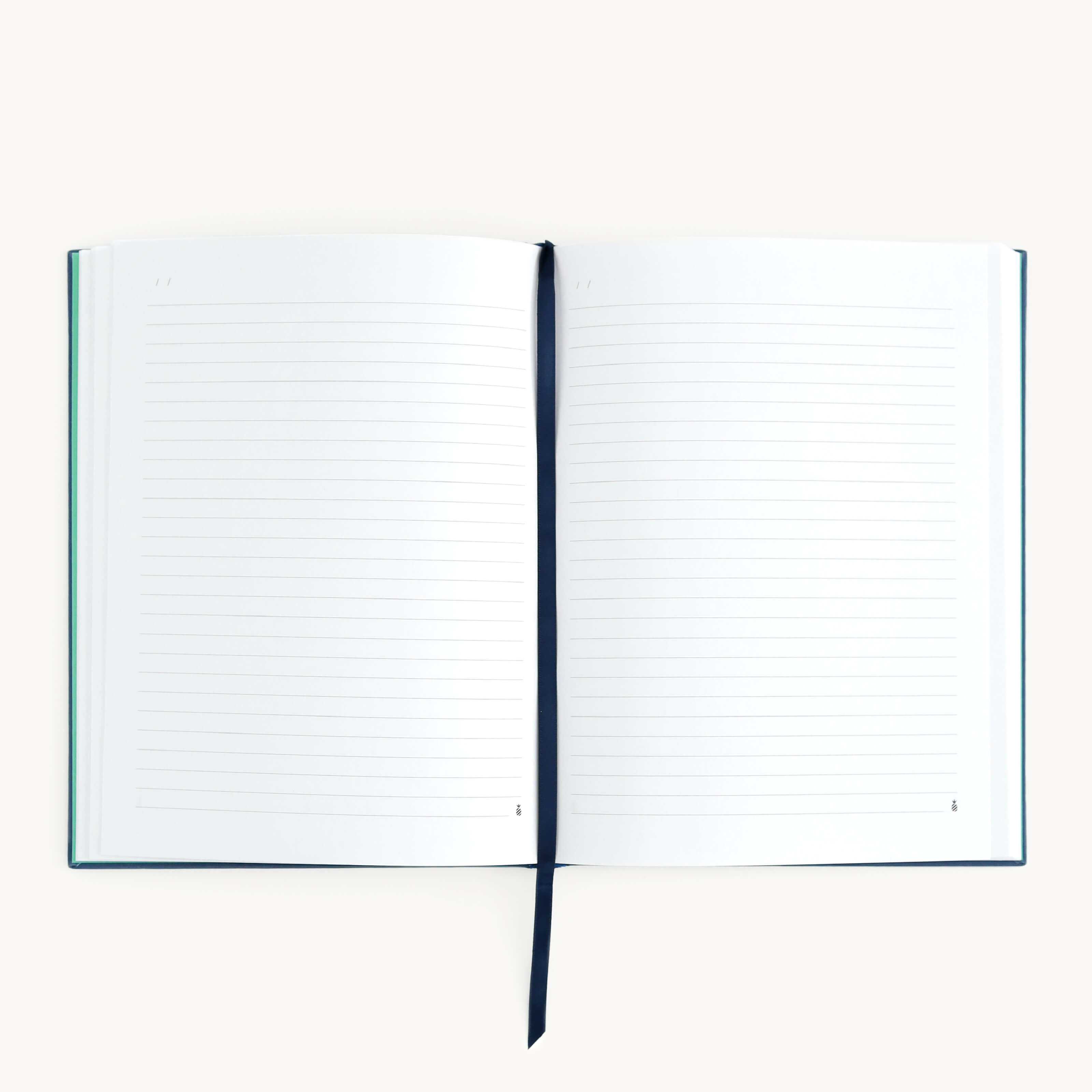 The Linen Journal - Navy by Simplified lies open with lined pages on a white surface, featuring a dark ribbon bookmark between pages. Its simple design with a visible spine invites reflection and creativity.