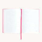 The Linen Journal - Raspberry by Simplified, featuring a pink ribbon bookmark and lined pages with pink edges, sits gracefully at the center against a white background, inviting moments of reflection and creativity to capture your thoughts.