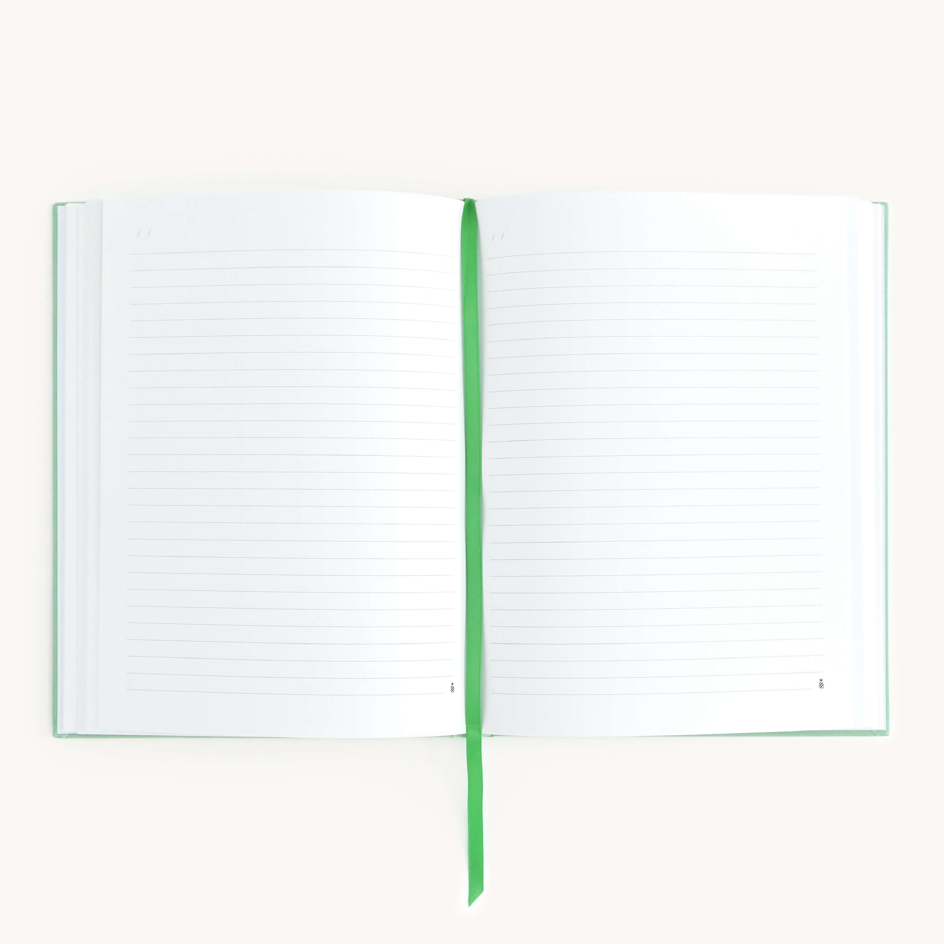 The Linen Journal - Sage by Simplified, featuring lined pages and a green bookmark ribbon at its center, invites creativity and reflection against a plain white backdrop.