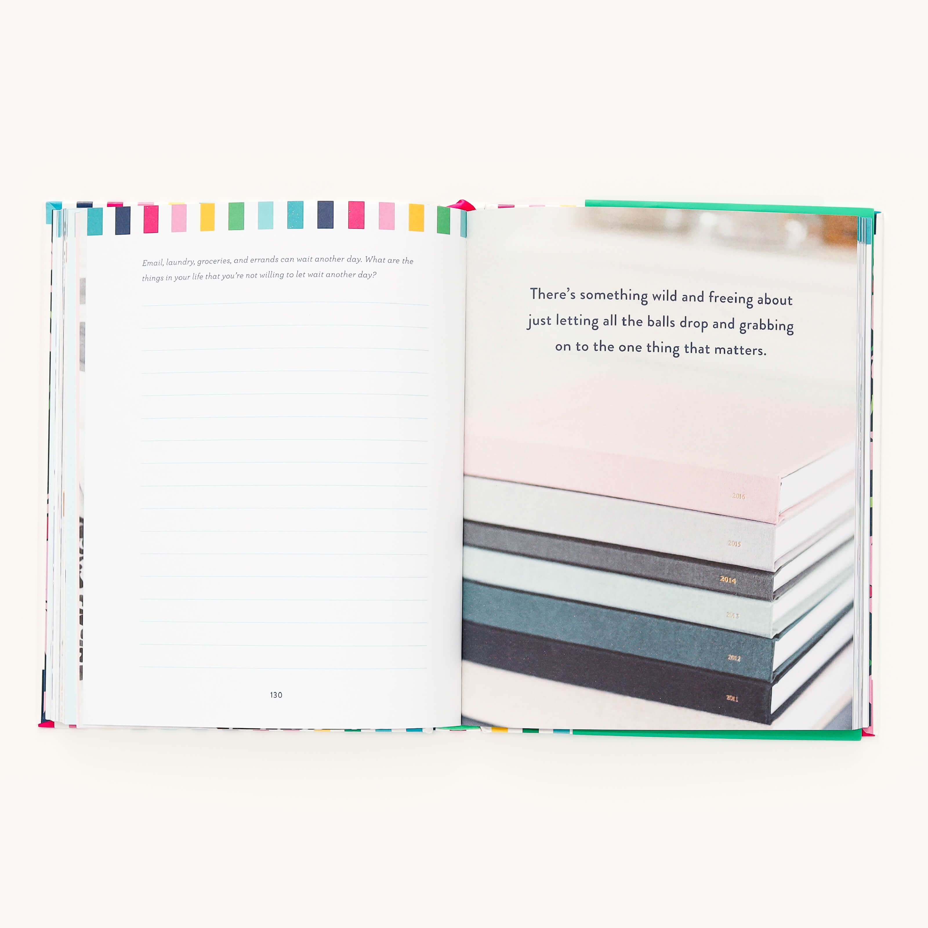 The A Standard of Grace journal by Emily Ley features a page with colorful edges, guided prompts for self-reflection, and a space for writing. The opposite side includes an inspirational quote about focusing on what matters, next to a stack of closed books.