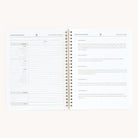 The Simplified Finances workbook by Simplified features an open spiral-bound design with a budget table on the left page for tracking income and expenses. The right page includes a Simplifying Challenge with checkboxes for tasks 1 to 5, ideal for managing finances.