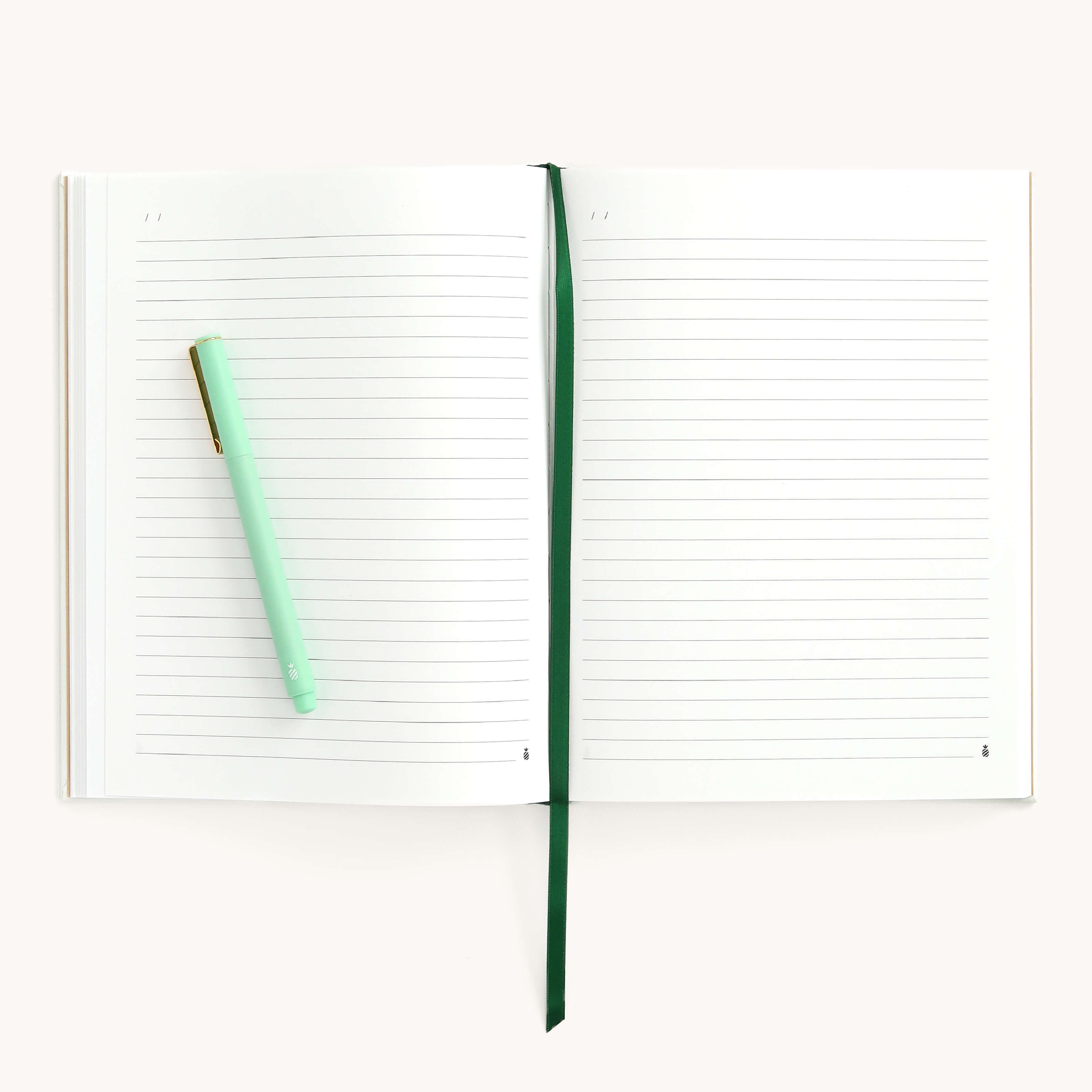 The Simplified Linen Journal - Gratitude lies open with lined pages and a linen hardcover, featuring a green ribbon bookmark in the center. A light green pen is positioned diagonally on the left page, all set against a plain white surface.