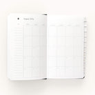 The 2024-2025 Daily Dapperdesk Planner - Black Tie by Simplified has a leatherette cover and opens to a monthly calendar view for August 2024, with lined note sections on the left and a dated grid on the right, plus edge tabs for easy navigation.