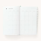 Monthly spread in the 2024-2025 Daily Dapperdesk Planner in the Sea Salt leatherette cover featuring mylar tabs with gold foil details.