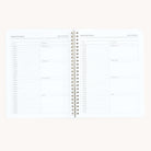 A visible open spiral-bound planner displays two pages, each featuring date sections, inspiration, to-do lists, gratitude, evening reflections, meals, and notes. Titled Simplified Travel Daily Trip Planner, it serves as a minimalist travel workbook for organizing your itineraries by Simplified.