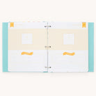 The Simplified Baby Book - Mint features an open scrapbook with light blue polka dot covers. Inside, cream-colored pages have yellow squares and banners for guided writing spaces. Each page has an About Your Baby section for personal details, perfect for a unique baby book experience.